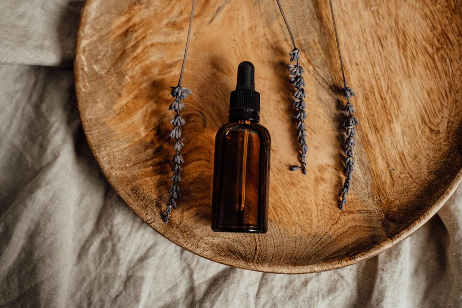 Amber dropper bottle of essential oil with dried lavender on a wooden tray